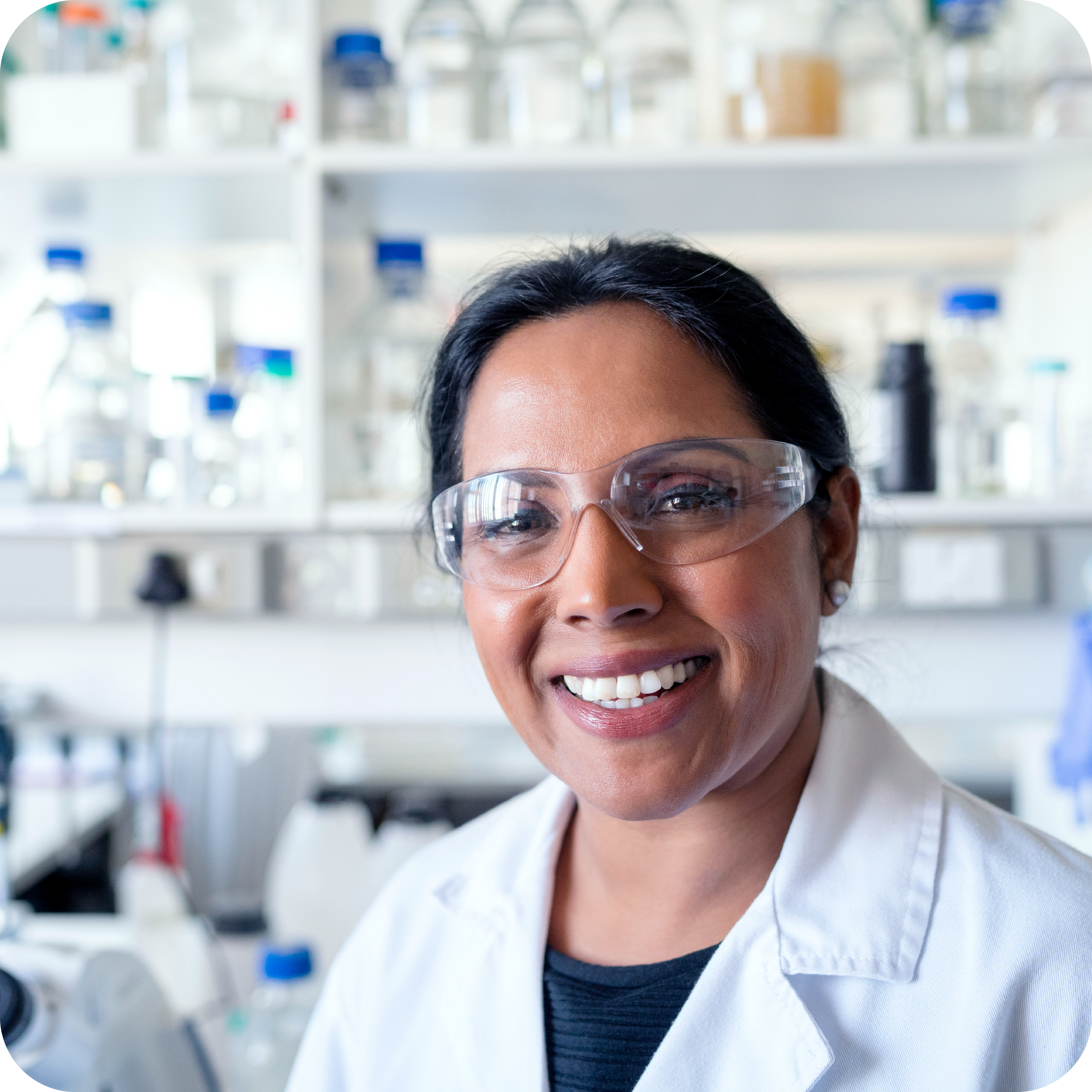A woman in a laboratory setting, smiling while dressed for work as a Pharmaceutical Scientist.