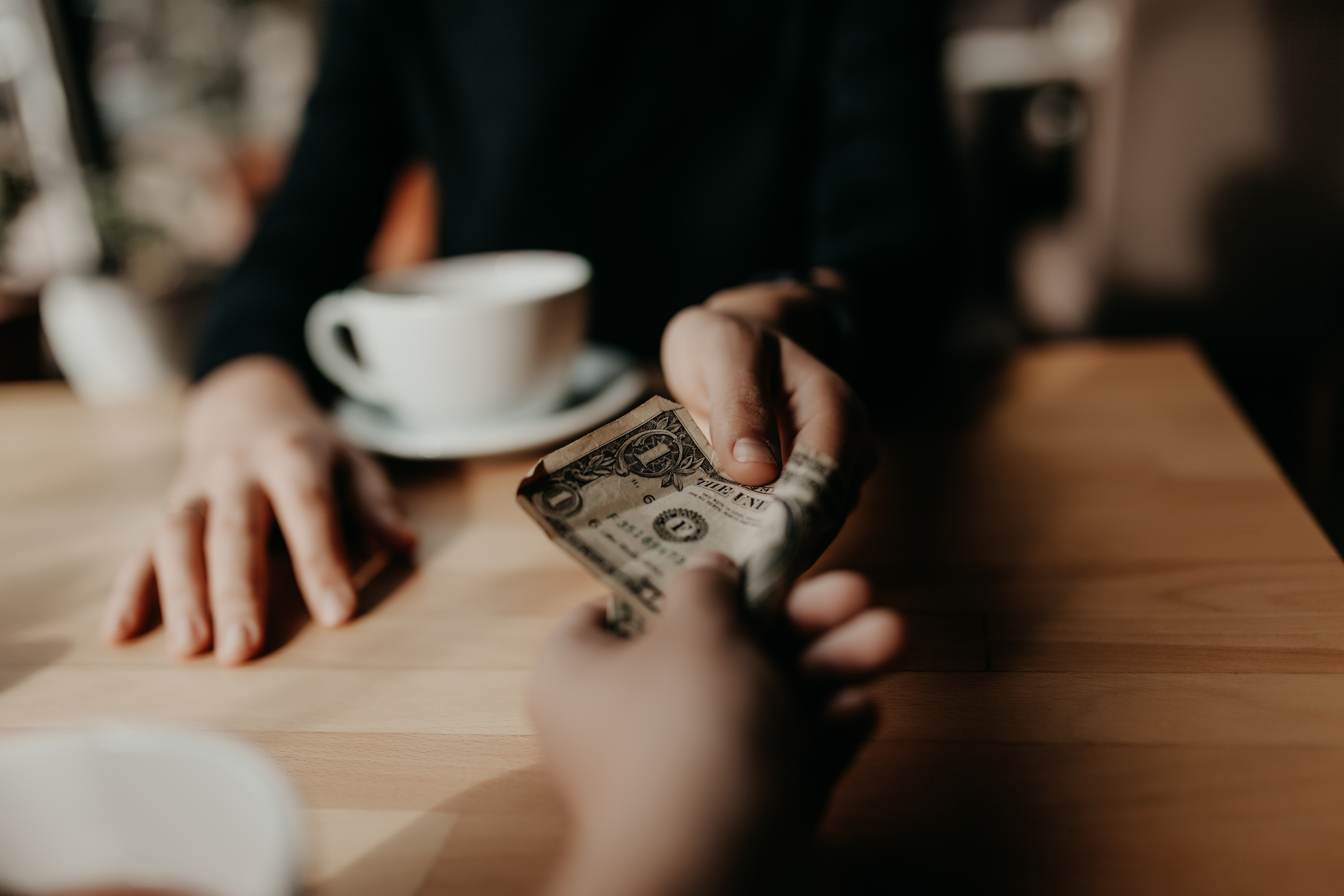 Two people exchange a dollar bill at a wooden table.