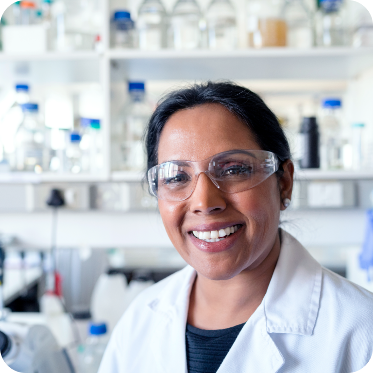 A woman in a laboratory setting, smiling while dressed for work as a Pharmaceutical Scientist.